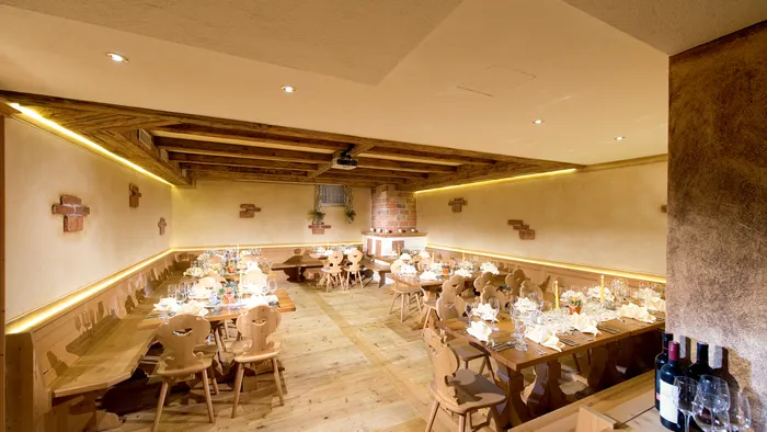 Rustikaler Speisesaal mit gedeckten Holztischen, Weinflaschen und warmer Beleuchtung